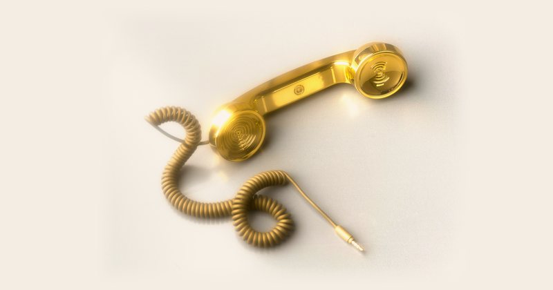 Guldfärgad telefonlur med spiralsladd mot ljus bakgrund